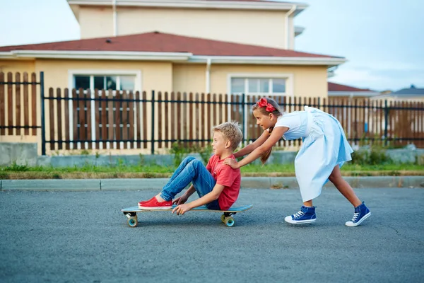 Мальчик толкает сестру сидя на скейтборде — стоковое фото