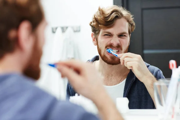 Mann schaut beim Zähneputzen in Spiegel — Stockfoto