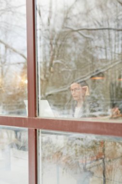 Konsantre üst düzey yöneticisi laptop iş e-postaları kontrol gözlük içinde panoramik kafe pencereden görüntüleme