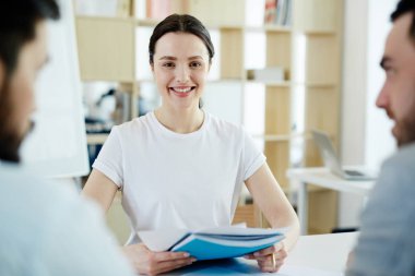 Müşterileri ile toplantı ve kameraya bakarak ofiste çalışan gülümseyen genç kadın portresi
