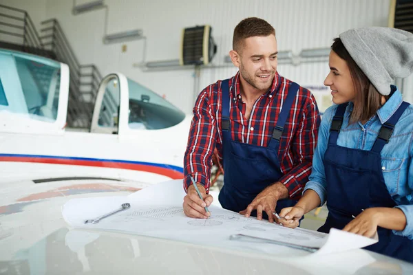 Two modern aircraft engineers, man and woman, discussing plane construction working with blueprints