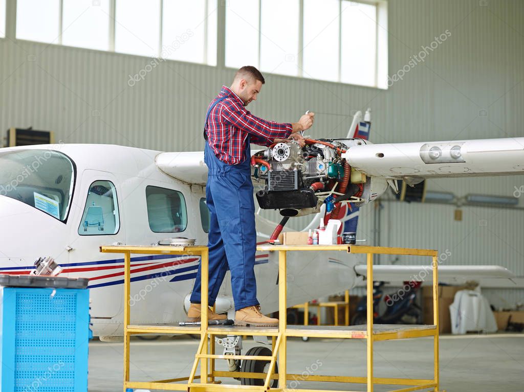 Young man in uniform of repairman fixing parts of jet engine