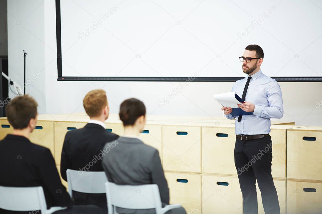 Confident young speaker presenting his point of view concerning company development while participating in business conference