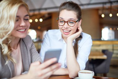 Having oyunculuk ile smartphone, arka plan üzerinde rahat küçük kahvehane, iç fotoğraflar bakarken neşeli genç arkadaşlar