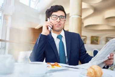 İstemci veya iş ortağına konuşuyor cellphone tarafından gazete ile meşgul bankacı