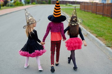 Little girls in witch costumes and hats walking away after halloween tricks clipart