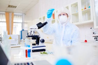 Filtre maskesi ve çok önemli deney taşıma sırasında konsantrasyon ile tüp seyir coverall giyen kadın laboratuvar işçi