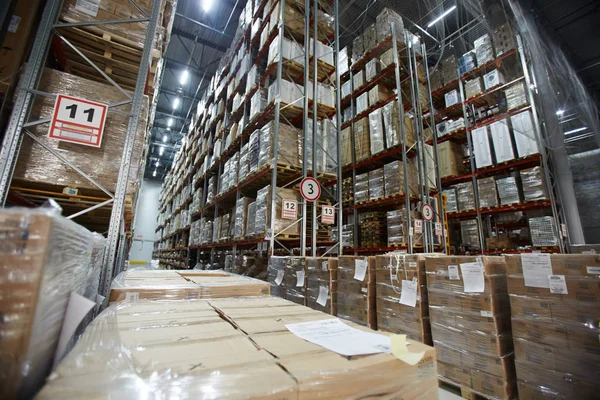 Large distribution warehouse with tall shelves and racks with packed goods in boxes