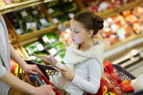 ショッピングカートと彼女自身を心に抱く彼女の両親食料品のスーパーで買い物しながらデジタル タブレットに座っている少女の肖像画 — ストック写真
