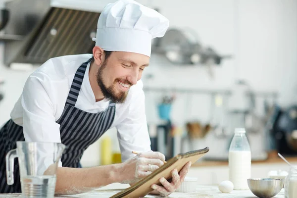 Glücklicher Koch Schreibt Etwas Notizblock Über Arbeitsplatz — Stockfoto
