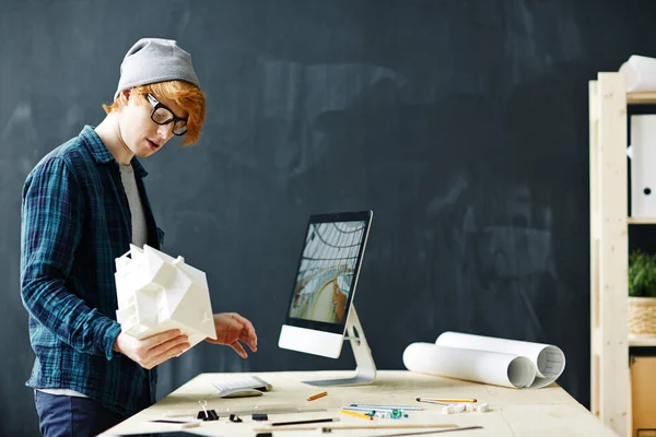 若い赤髪建築家モデルを保持していると設計図や背景に黒板のオフィスで各種物資を職場で立っている現代のコンピューターを使用しての側面ビュー肖像画 — ストック写真