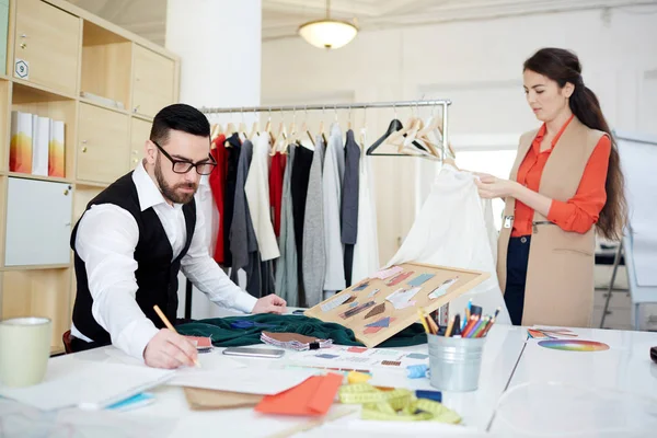 Serious Couturier Dibujando Bocetos Moda Mientras Asistente Trabaja Con Ropa — Foto de Stock