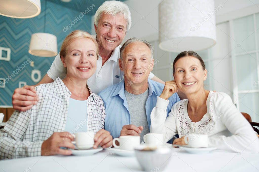 Company of affectionate senior friends spending time in cafe at leisure