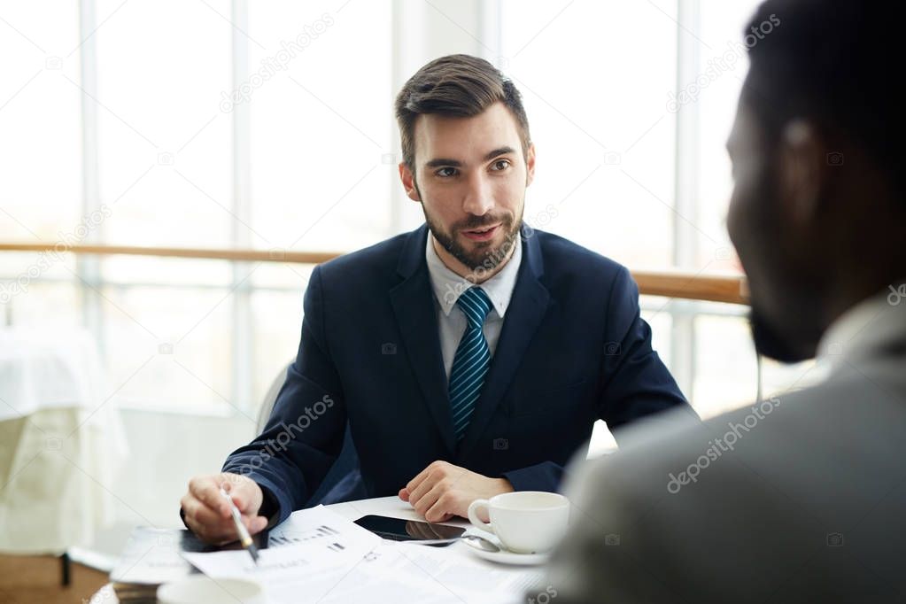 Portrait of two businessmen, one of them African, negotiating conditions while discussing deal during meeting in cafe