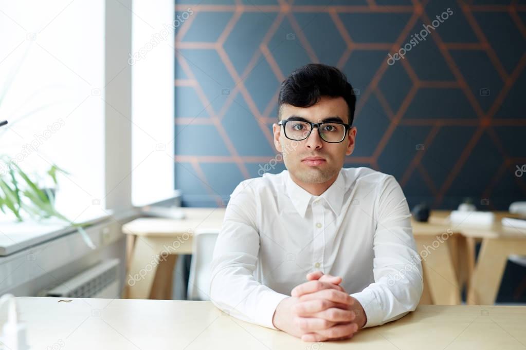 Businessman in eyeglasses and white shirt sitting by desk