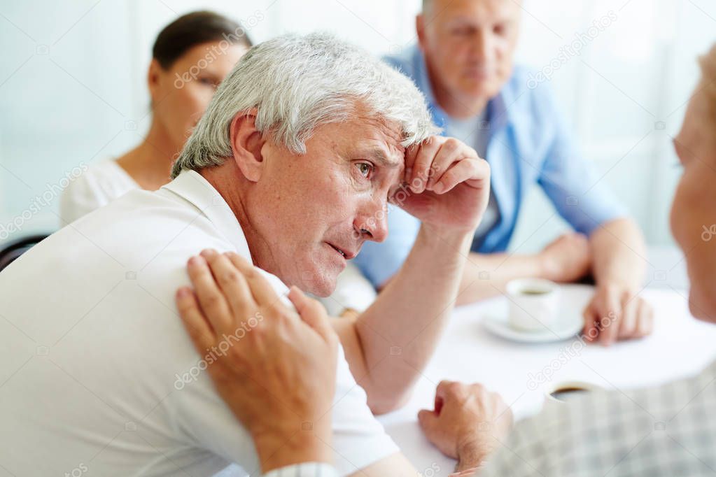 Upset retired man talking to supporting friend and sharing his troubles