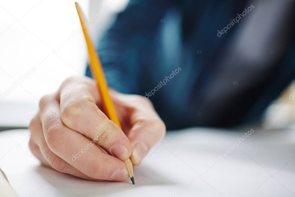 Closeup of male hand holding pencil on blank paper, drawing or writing