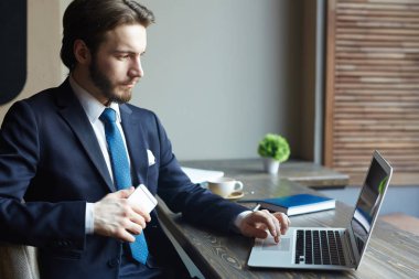 Yan görünümü ekrana bakarak laptop ve smartphone Cafe, kahve molası sırasında tahta masada çalışma yakışıklı zarif işadamı portresi