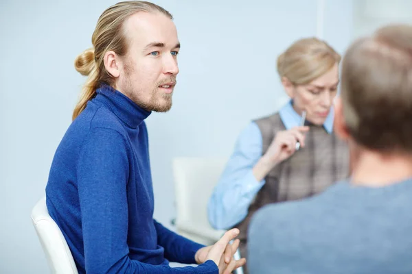 长头发和休闲衣服的年轻大胡子的画像坐在小组治疗会议与心理学家和其他病人听他的故事 — 图库照片