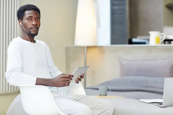 自信的非裔美国自由职业摄影师坐在舒适的椅子上拍照 使用数字平板电脑 背景的现代工作室公寓室内 — 图库照片