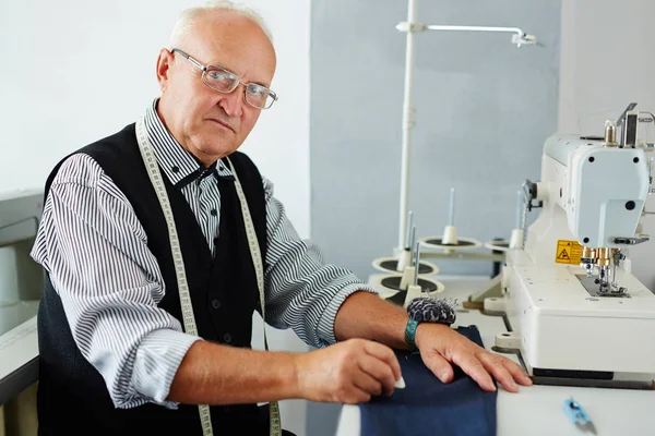 在裁缝工作室做衣服的老人画像在缝纫机和看照相机 — 图库照片