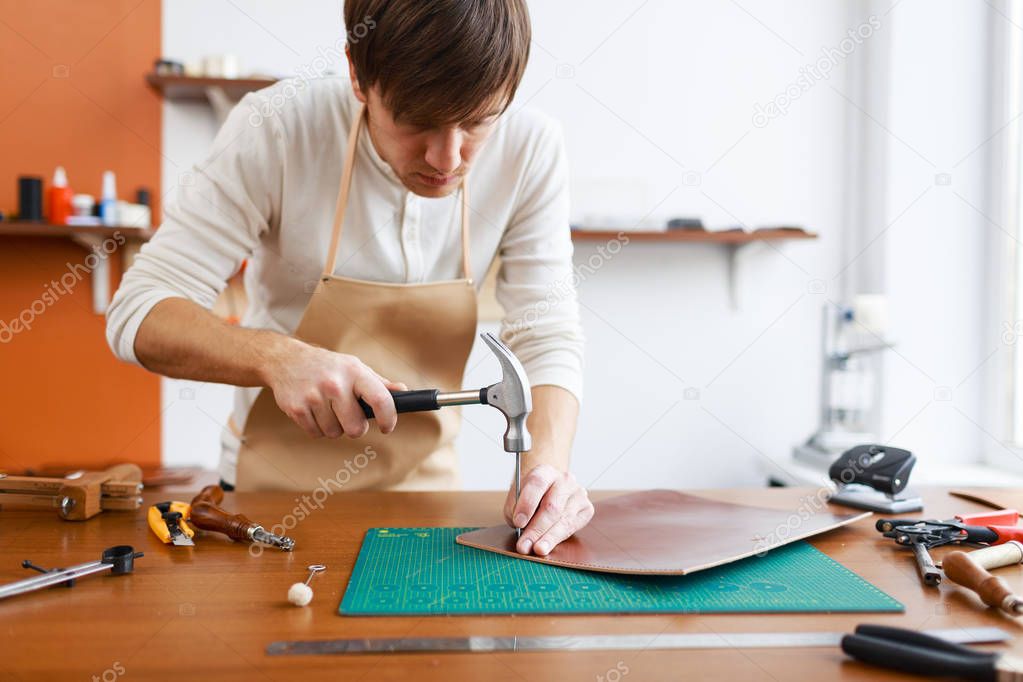 Modern upholsterer with hammer and nail piercing piece of leather