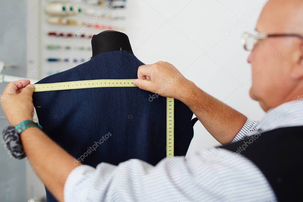 Closeup portrait of grey haired old man measuring back on mannequin in traditional tailoring studio