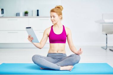 Yoga yaparken uygun kırmızı saçlı kadın portresi egzersizleri evde: bacaklar ile oturma geçti lotus pozisyonu ve okuma e-kitap