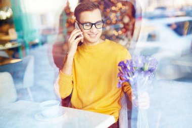 Süsen buket Tarih için beklerken kafede telefonla konuşan gülümseyen genç adam portresi
