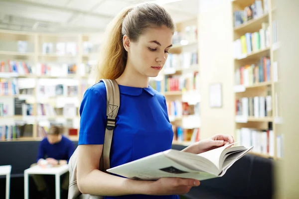 図書館の本棚のそばに立って 試験の準備で本を読んでかなり若い女性の肖像画 — ストック写真