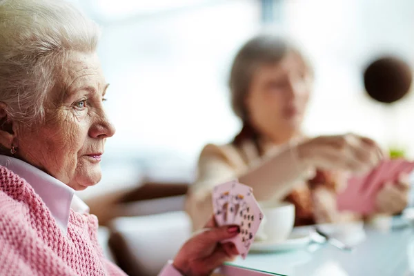深蓝色眼睛的忧郁的老年妇女的外形视图坐在桌上和她的女性朋友打牌 — 图库照片