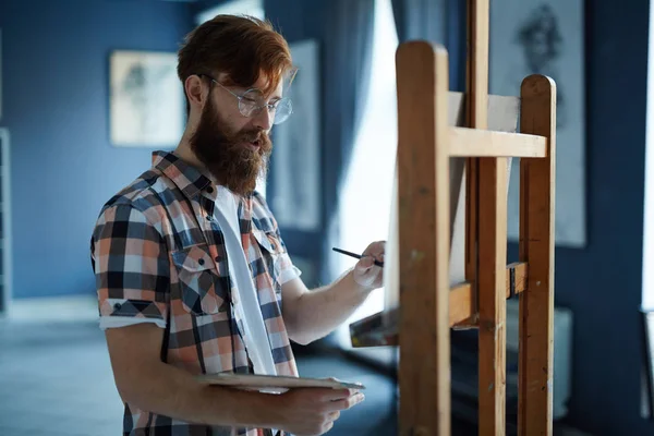 焦点を当てた現代アーティスト ひげメガネの冴えない男アート スタジオでキャンバスに絵を描いての肖像画 — ストック写真