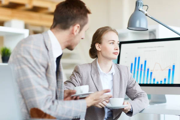 Professional colleagues in suits gathered together at open plan office and having small talk while enjoying fragrant coffee, pretty manager with deep blue eyes looking into distance pensively