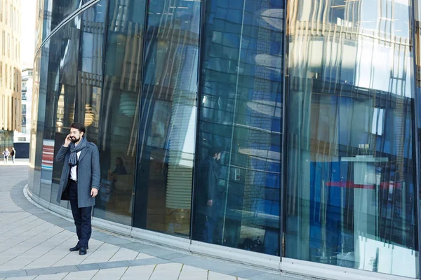 Paltonu ve kaşkolünü modern ofis bina ve iş ortağı smartphone üzerinde konuşurken ayakta giyen sakallı orta yaşlı girişimci tam uzunlukta portresi