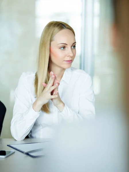 在现代办公室坐在会议桌上的漂亮金发女郎的肖像 微笑着 聚精会神地听同事们讲话 — 图库照片