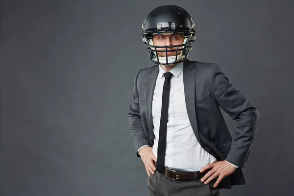 アメリカン フットボールのヘルメットと灰色の背景に対して腰に手で立っていると離れてカメラ目線のスーツを着て自信を持っての実業家の肖像画 — ストック写真