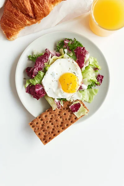 直接以上观点开胃早餐 不同类型的生菜 一个煎蛋和薄脆 玻璃新鲜橙汁和美味的牛角面包的瓷板 — 图库照片
