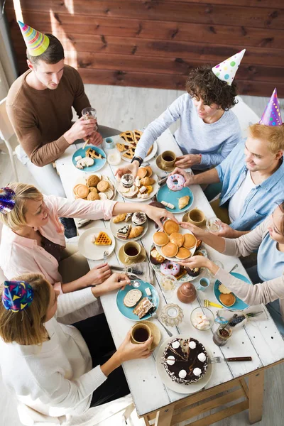 テーブルでお祝い食糧を持つ誕生日キャップに複数の友人 — ストック写真