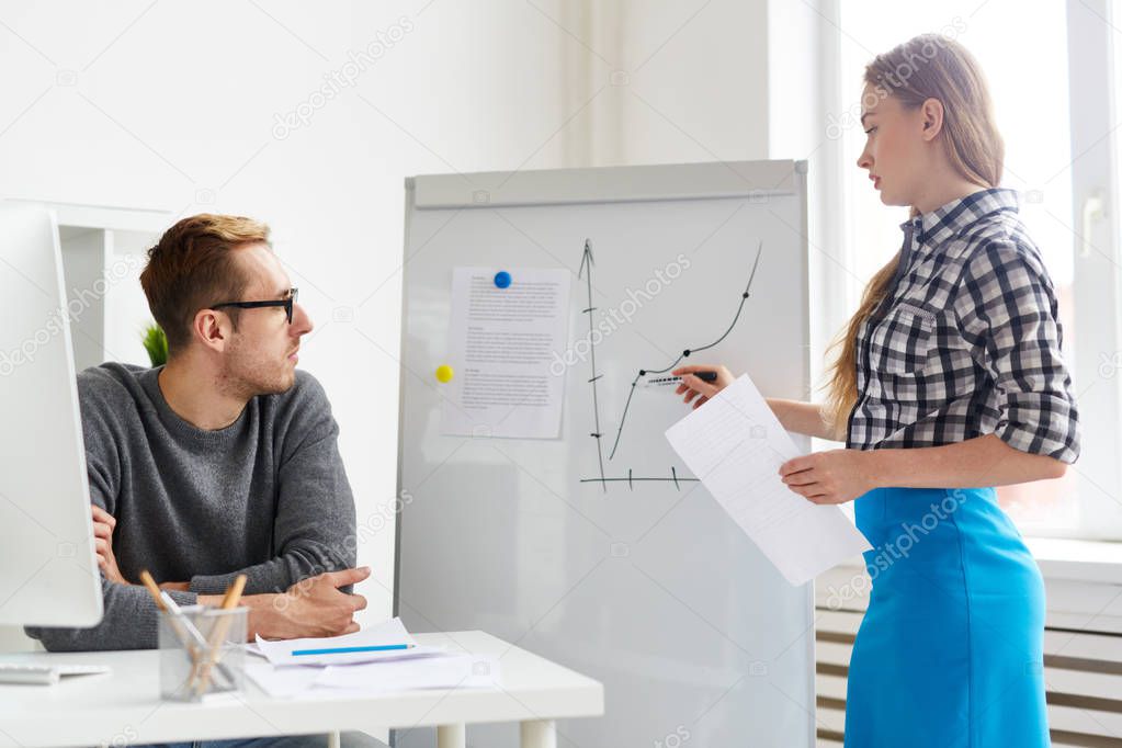 Young economist making presentation of financial changes on market on whiteboard
