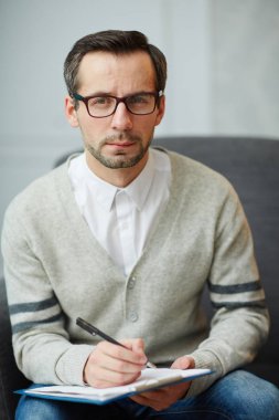 Erkek psikiyatrist notlar yaparken kameraya bakıyor