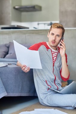 Çağdaş ev ofis çalışanı ile smartphone ile konuşurken kameraya bakarak kağıtları