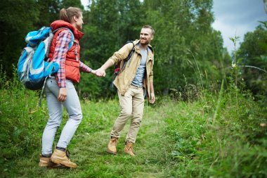 Genç backpackers yeşil çim yürürken konuşmak