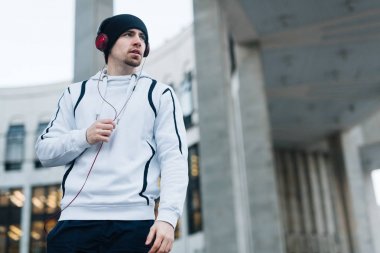 Aktif genç adam hoodie ve kentsel ortamda müzik dinlemek bere