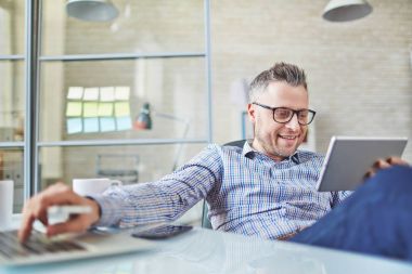 Makale, o aynı zamanda dizüstü bilgisayar kullanmaya çalışan okumak için dijital tablet kullanarak pozitif orta yaşlı işadamı