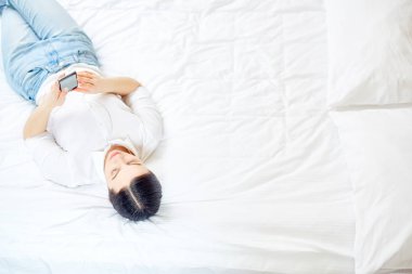 Genç kadın yatakta dinlenirken Smartphone içinde ileti