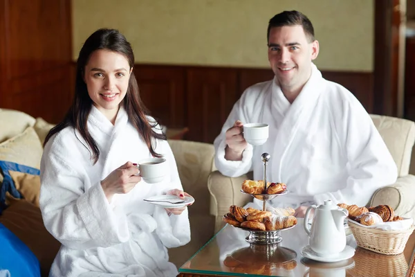 年轻夫妇在浴袍有咖啡与包子在旅馆房间 — 图库照片