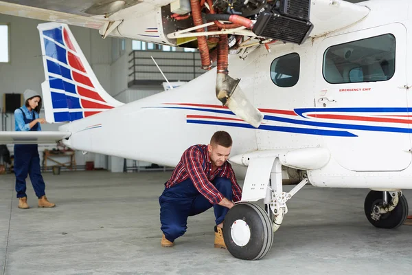 Airplane service crew repairing plane in hangar:  two modern mechanics, man and woman, fixing jet plane