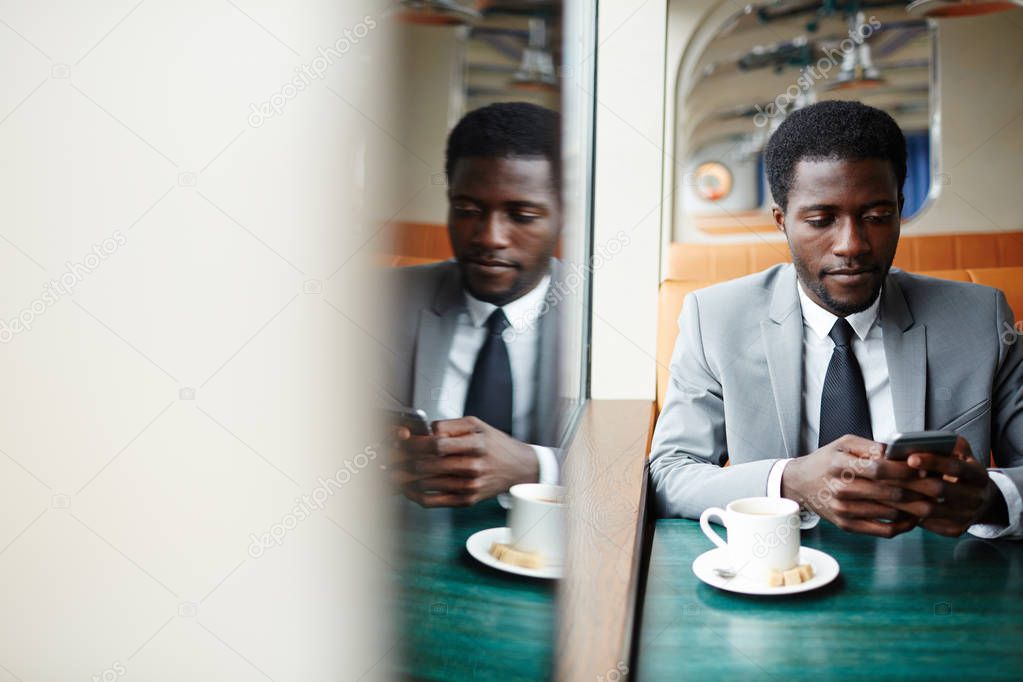 Elegant man sitting in steamship cafe and texting in smartphone