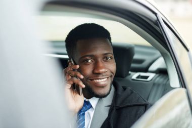 Gülümseyerek, arabada telefon görüşmesi yaparken kameraya bakarak başarılı Afrikalı-Amerikalı işadamı portresi
