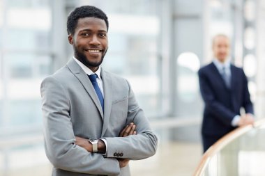 Gülümseyen portresi Afrikalı - Amerikalı işadamı kameraya güvenle silahlarla seyir geçti ikinci adam arka planda bina modern ofis